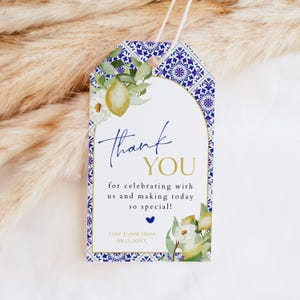 May include: A decorative gift tag with a blue and white tile pattern border. The tag features a lemon and floral design with the words "thank you" in navy and gold. The text reads "for celebrating with us and making today so special!"