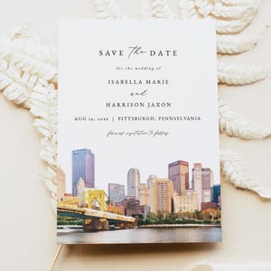 May include: A white wedding invitation with the text "SAVE THE DATE" and the names Isabella Marie and Harrison Jaxon. The date and location are also included. The bottom features a watercolor painting of a city skyline.