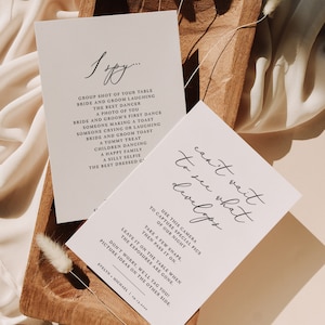 Puede incluir: Dos tarjetas blancas con texto negro. La primera tarjeta dice "I Spy..." y enumera una serie de cosas para fotografiar en una boda. La segunda tarjeta dice "Can't wait to see what develops" e instruye a los invitados a usar una cámara desechable para tomar fotos en la boda.