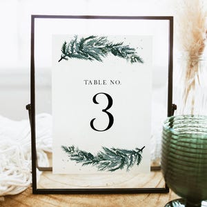 May include: A white card with a black frame, featuring a watercolor illustration of green pine branches and the text "TABLE NO. 3".