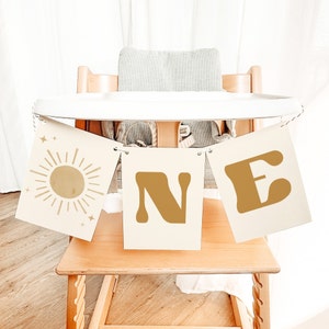 May include: A white high chair with a banner that says "ONE" in gold letters. The banner is decorated with a sun and stars.