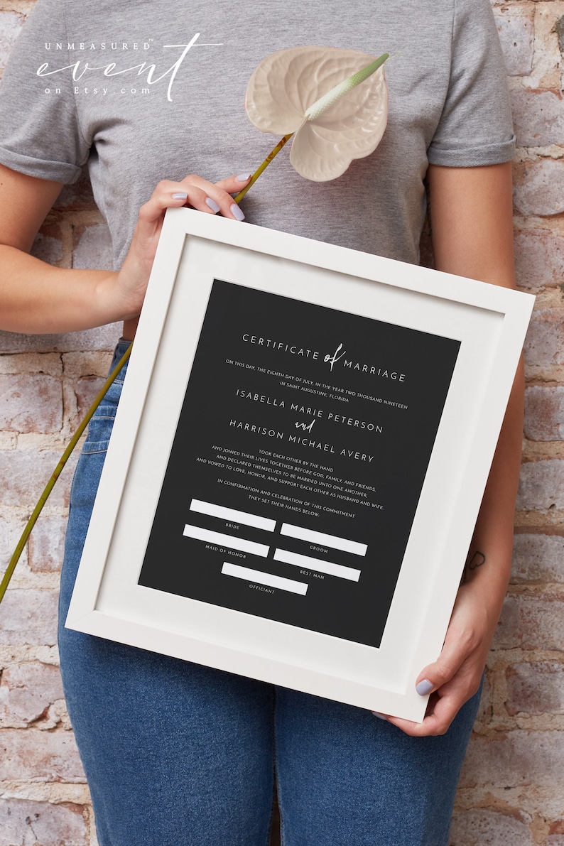 May include: A framed marriage certificate with a black background and white text. The certificate includes the names Isabella Marie Peterson and Harrison Michael Avery. The frame is white.