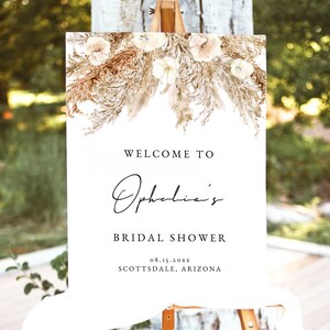 May include: A white welcome sign with a floral design at the top. The sign reads "Welcome to Ophelia's Bridal Shower 08.15.20XX Scottsdale, Arizona".