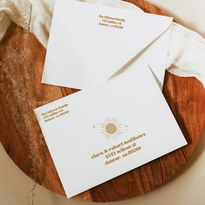 May include: Two white envelopes with a gold sun graphic and text. The text on the top envelope reads "the bilyvau family 543 miller rd denver, co 80210". The text on the bottom envelope reads "clara & robert maffhews 1543 wilcox st denver, co 80210".