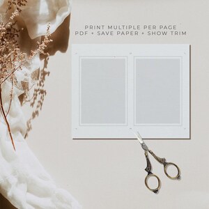 May include: A white sheet of paper with two rectangular frames, each with a white background. The text "PRINT MULTIPLE PER PAGE - PDF + SAVE PAPER + SHOW TRIM" is printed at the top of the page. A pair of gold-colored scissors is lying on the page below the frames.