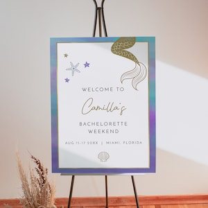 May include: Welcome to Camilla's Bachelorette Weekend sign with a mermaid tail and starfish design. The sign is on a wooden easel and has a purple and blue ombre background. The text on the sign reads: "Welcome to Camilla's Bachelorette Weekend Aug 15-17 20XX | Miami, Florida"