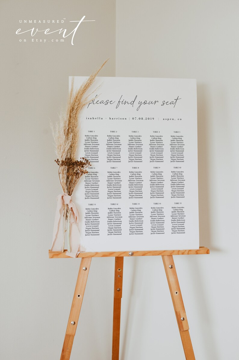 May include: A white seating chart with the text "please find your seat" at the top. The chart lists names for each table number, from table 1 to table 15. The chart is on an easel with a dried flower arrangement.