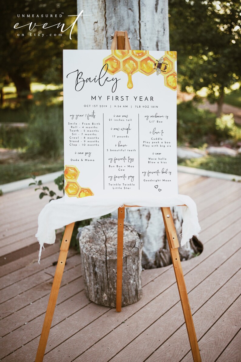 May include: A watercolor illustration of a honeycomb with a dripping honey drop and a bee. The illustration is on a white background with black text that reads "Bailey My First Year Oct 1st 2019 9:54 AM 7LB 9OZ 18IN" and lists milestones for a baby's first year, including age, height, weight, and favorite things.