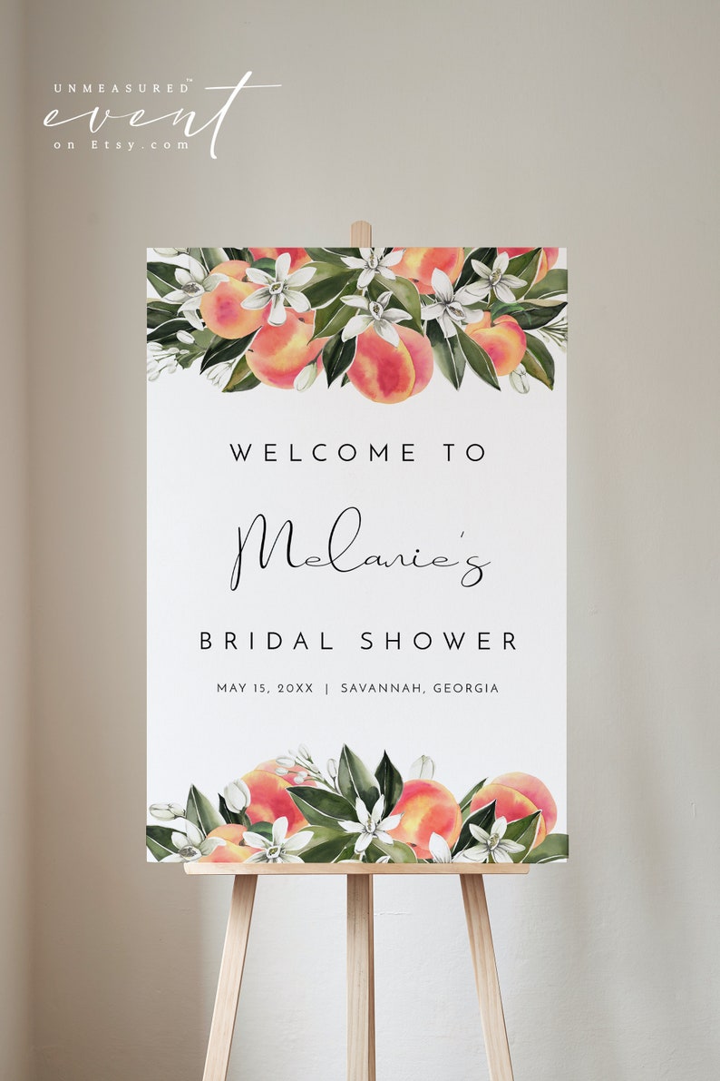 May include: A white sign with peach blossoms and peaches on top and the text "WELCOME TO Melanie's BRIDAL SHOWER MAY 15, 20XX SAVANNAH, GEORGIA".