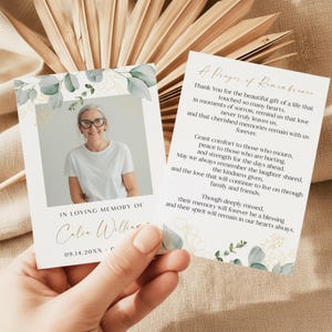 May include: A memorial card featuring a photo of a woman with glasses, surrounded by eucalyptus and gold accents. The card includes the text "In Loving Memory Of" and a name, along with a date. A second card displays a poem.