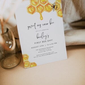 May include: A white invitation card with a watercolor illustration of a honeycomb and a bee. The text on the card reads "sweet as can bee" and "Join us in celebrating Bailey's First Bee-Day!" The invitation details the date, time, and location of the event. RSVP information is also included.