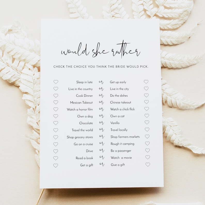 Op de afbeelding: Een printbaar bruidsdouchespel met de tekst "would she rather" en een lijst van 14 vragen met twee keuzes per vraag. De keuzes worden gepresenteerd in een zwart-wit ontwerp met een hartje naast elke keuze.