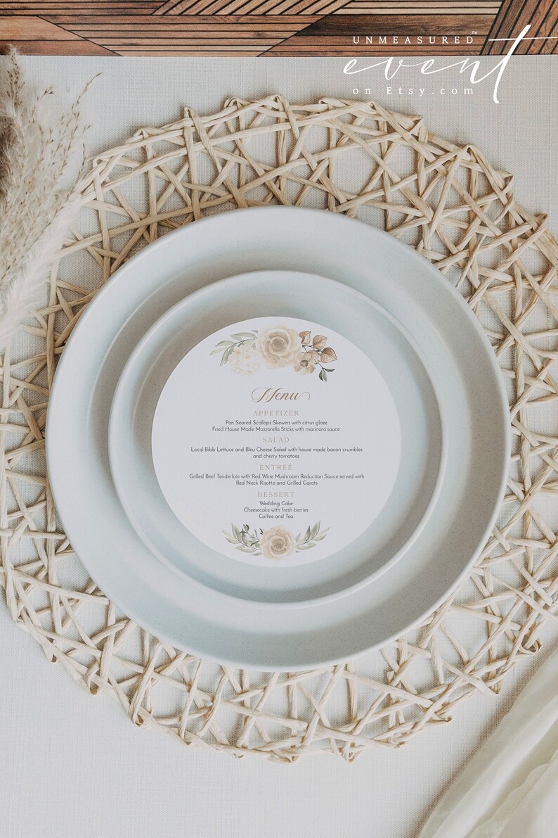 Op de afbeelding: Een ronde lichtblauwe plaat met een kleinere ronde plaat erop. De kleinere plaat heeft een witte achtergrond met een bloemenpatroon en een menu erop gedrukt. Het menu bevat opties voor voorgerechten, salade, hoofdgerecht en dessert. De platen liggen op een geweven placemat.