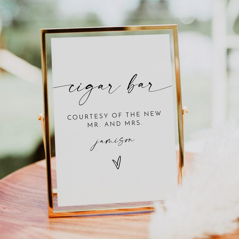 May include: A white sign with black text in a gold frame that reads "cigar bar" and "courtesy of the new mr. and mrs. jamison".