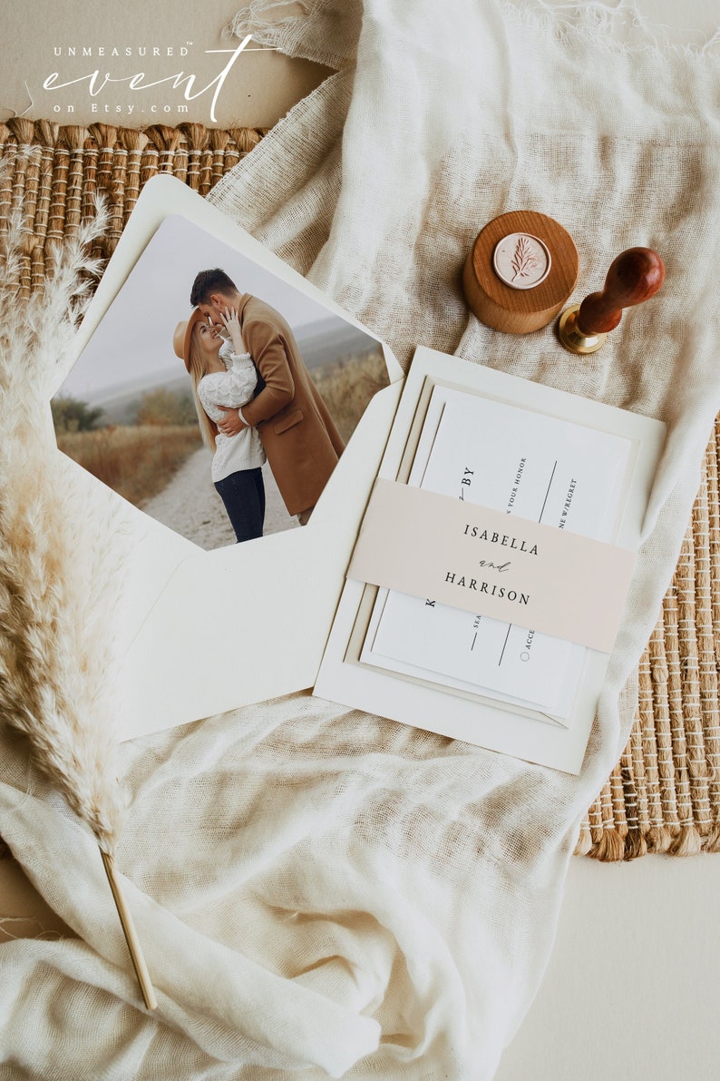 May include: A wedding invitation suite with a blush pink ribbon and a photo of a couple in a field. The invitation reads "By Isabella and Harrison".