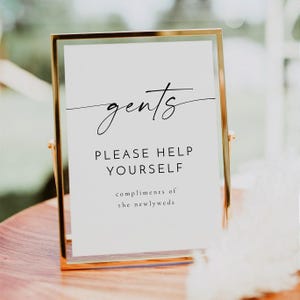 以下が含まれることがあります： 「gents」と cursive で書かれた金の額縁の看板。看板には「ご自由にお取りください。新郎新婦より」と書かれています。