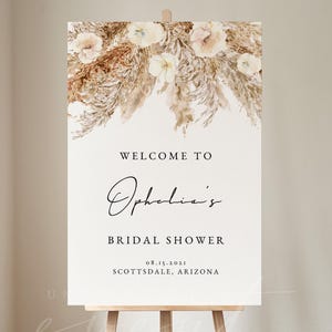 May include: Welcome to Ophelia's Bridal Shower sign with a watercolor background of dried flowers and pampas grass. The text is in black and the date is 08.15.2021. The location is Scottsdale, Arizona.