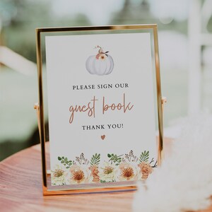 May include: A framed sign with gold trim, displaying the text "PLEASE SIGN OUR guest book THANK YOU!" in a decorative font. The sign features a watercolor pumpkin and floral design, suitable for a wedding or event.