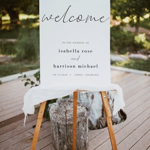 May include: White wedding welcome sign with black calligraphy text. The sign reads "Welcome to the wedding of Isabella Rose and Harrison Michael 08.15.2020 | Aspen, Colorado".