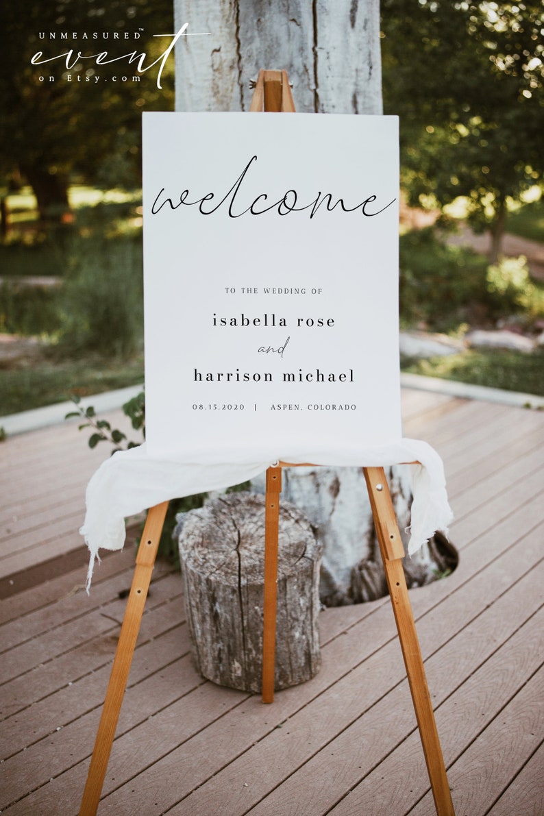 May include: White wedding welcome sign with black calligraphy text. The sign reads "Welcome to the wedding of Isabella Rose and Harrison Michael 08.15.2020 | Aspen, Colorado".