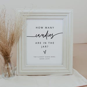 Puede incluir: Un cartel enmarcado en blanco con texto negro que dice "HOW MANY candies ARE IN THE JAR?" con un s&iacute;mbolo de coraz&oacute;n y "THE CLOSEST GUESS WINS. GOOD LUCK!"