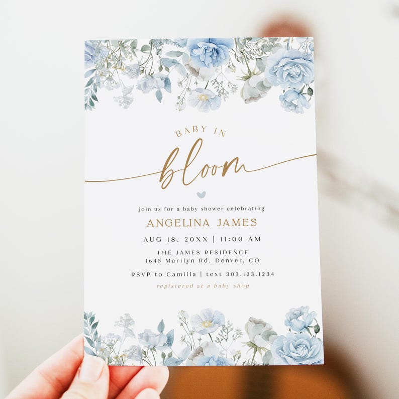 May include: Baby shower invitation with floral design. The invitation features the words "Baby in Bloom" in gold script, with light blue floral accents. The invitation includes the event details.