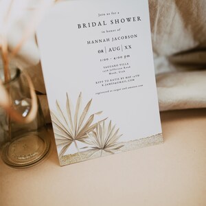 May include: A white card with a gold border and a palm leaf design. The card is an invitation to a bridal shower for Hannah Jacobson on August 8th at 1:00 pm to 4:00 pm at Saguaro Villa, 1378 Jefferson Road, Moab, Utah. RSVP to Katie by May 1st at K.JAMES@GMAIL.COM. Registered at Target and Amazon.com.