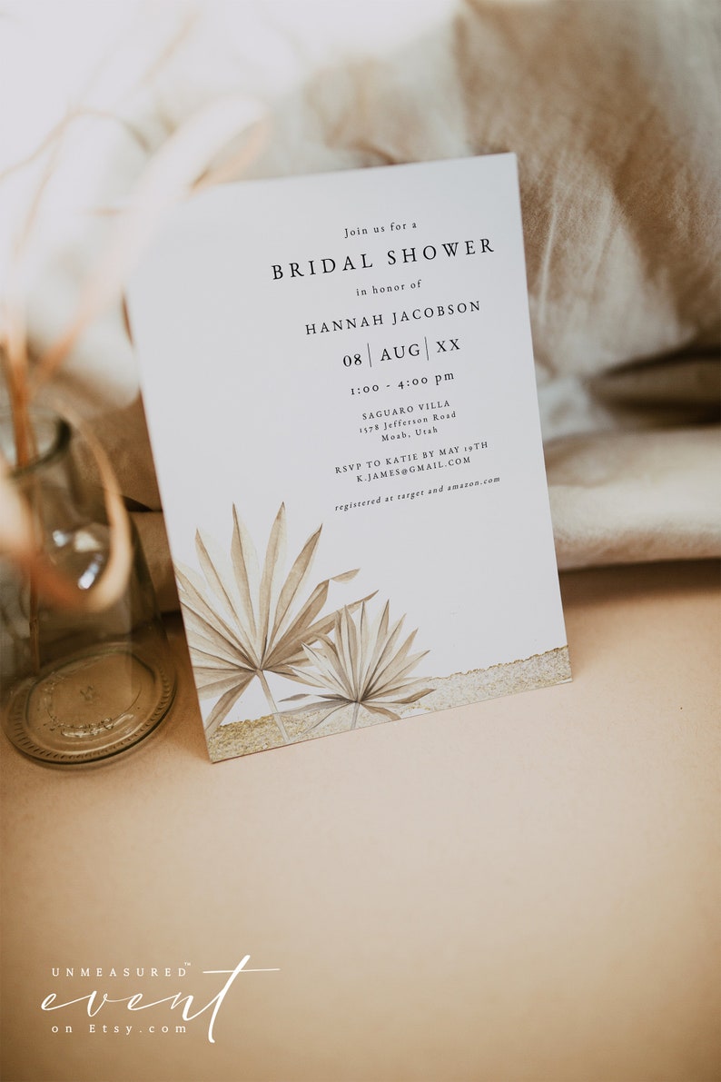 May include: A white card with a gold border and a palm leaf design. The card is an invitation to a bridal shower for Hannah Jacobson on August 8th at 1:00 pm to 4:00 pm at Saguaro Villa, 1378 Jefferson Road, Moab, Utah. RSVP to Katie by May 1st at K.JAMES@GMAIL.COM. Registered at Target and Amazon.com.