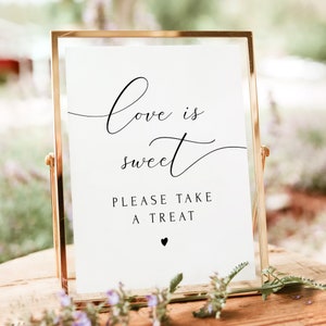 May include: A gold-framed sign with the text "Love is sweet" and "Please take a treat" with a small heart at the bottom.
