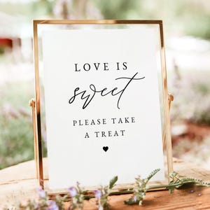 May include: A gold-framed sign with the text "Love is sweet. Please take a treat." and a small black heart at the bottom.