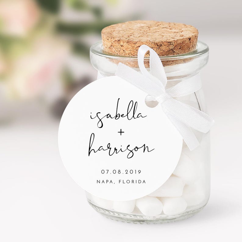 May include: White round favor tag with black calligraphy text that reads "isabella + harrison" and the date "07.08.2019" and location "NAPA, FLORIDA".