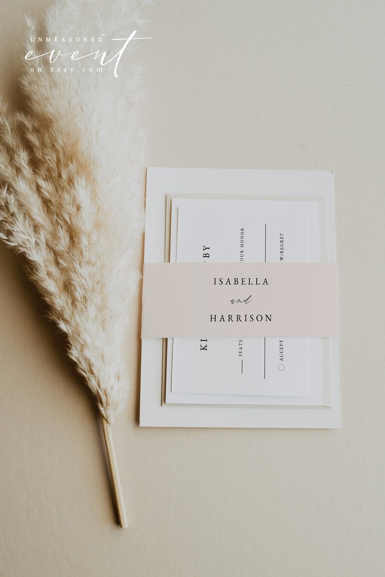 May include: A white wedding invitation with a blush pink ribbon. The ribbon has the text "ISABELLA and HARRISON" printed on it. The invitation also has the text "BY OUR HONOR" and "W/REGRET" printed on it.