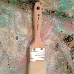 May include: A paint brush with a light wooden handle and a rectangular head of white bristles. The handle has a hole for hanging and the brand name "Zibra" is printed on the handle. The metal ferrule is silver.