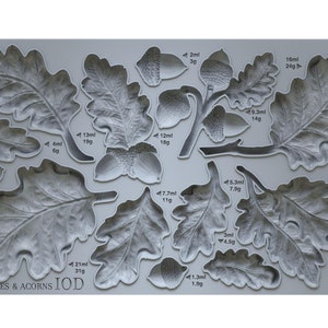 May include: A gray silicone mold with 12 different shapes of oak leaves and acorns. The mold is labeled "OAK LEAVES & ACORNS IOD" and each shape has measurements in milliliters and grams.