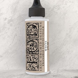 May include: A white, erasable liquid chalk bottle with a black cap. The label features the text "Iron Orchid Designs" and decorative black letter designs. The bottle contains 2 fl oz of white chalk.