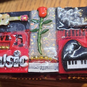 May include: A red, black, and white box with a collage of images. The box has a black background with a red border. The images include a ukulele, a rose, a piano, and the words "Live Music".