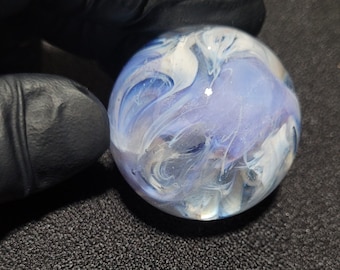 May include: A blue and white glass marble with swirling patterns. The marble is round and smooth.