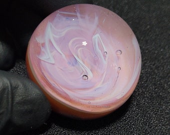 May include: A pink and white glass marble with swirls of white paint and air bubbles.