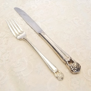 May include: A silver fork and knife with ornate floral designs on the handles. The fork has four tines and the knife has a serrated blade.