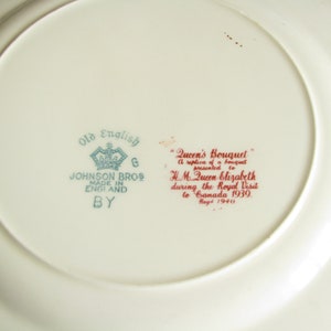 May include: A white ceramic plate with a blue and green design that says "Old English" and "Johnson Bros Made in England By". The plate also has a red inscription that says "Queen's Bouquet A replica of a bouquet presented to H.M. Queen Elizabeth during the Royal Visit to Canada 1939. Reg'd 1940."
