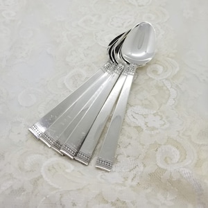 May include: Set of six silver teaspoons with a decorative beaded pattern on the handle. The spoons are arranged in a fan shape.