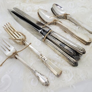 Op de afbeelding: Een set vintage bestek, inclusief vorken, messen en lepels, gebonden met touw. Het bestek is gemaakt van gepolijst zilver en heeft sierlijke ontwerpen.