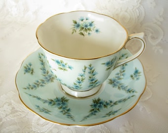 May include: A delicate teacup and saucer set with a light blue background and a floral pattern of blue flowers. The set has a gold trim around the edges.