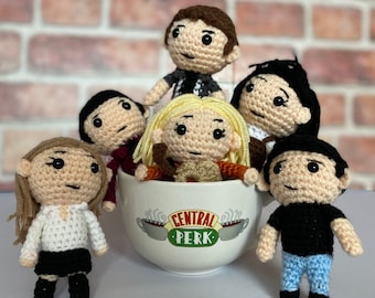 May include: Six crocheted figures of the characters from the TV show Friends, sitting around a Central Perk coffee mug. The figures are all wearing their signature outfits from the show.
