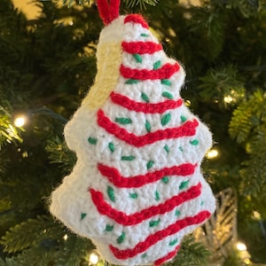 May include: A crocheted Christmas tree ornament with red and white stripes and green sprinkles. The ornament is hanging on a Christmas tree.
