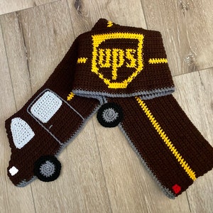 Könnte beinhalten: Ein brauner und gelber Häkel-Schal mit einem UPS-Logo und einem braunen LKW-Design. Der LKW hat weiße Fenster und Räder.