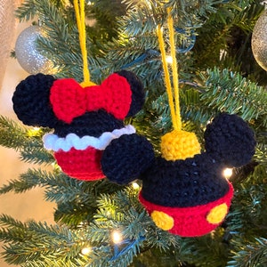 Könnte beinhalten: Zwei gehäkelte Weihnachtsbaumschmuckstücke, eines mit Mickey Mouse und eines mit Minnie Mouse. Mickey Mouse ist rot, schwarz und gelb, während Minnie Mouse rot, schwarz und weiß ist.