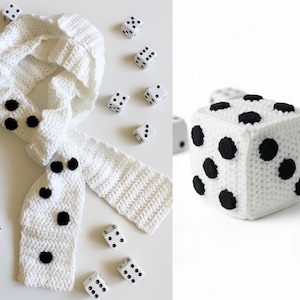 Op de afbeelding: Een witte gehaakte sjaal met grote zwarte stippen, die op dobbelstenen lijken. Verspreid liggen verschillende witte dobbelstenen met zwarte stippen. Er is ook een grote, kubusvormige gehaakte dobbelsteen aanwezig.