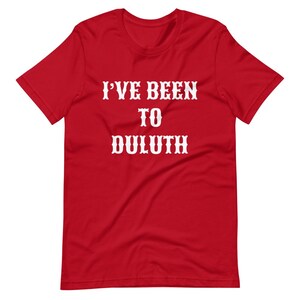 以下が含まれることがあります： 白い文字で「I'VE BEEN TO DULUTH」と書かれた赤い半袖Tシャツです。