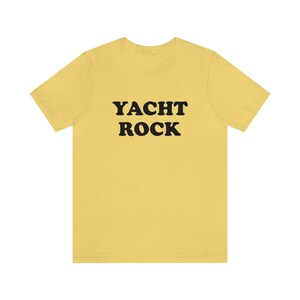 Puede incluir: Una camiseta amarilla con el texto "YACHT ROCK" impreso en negro.